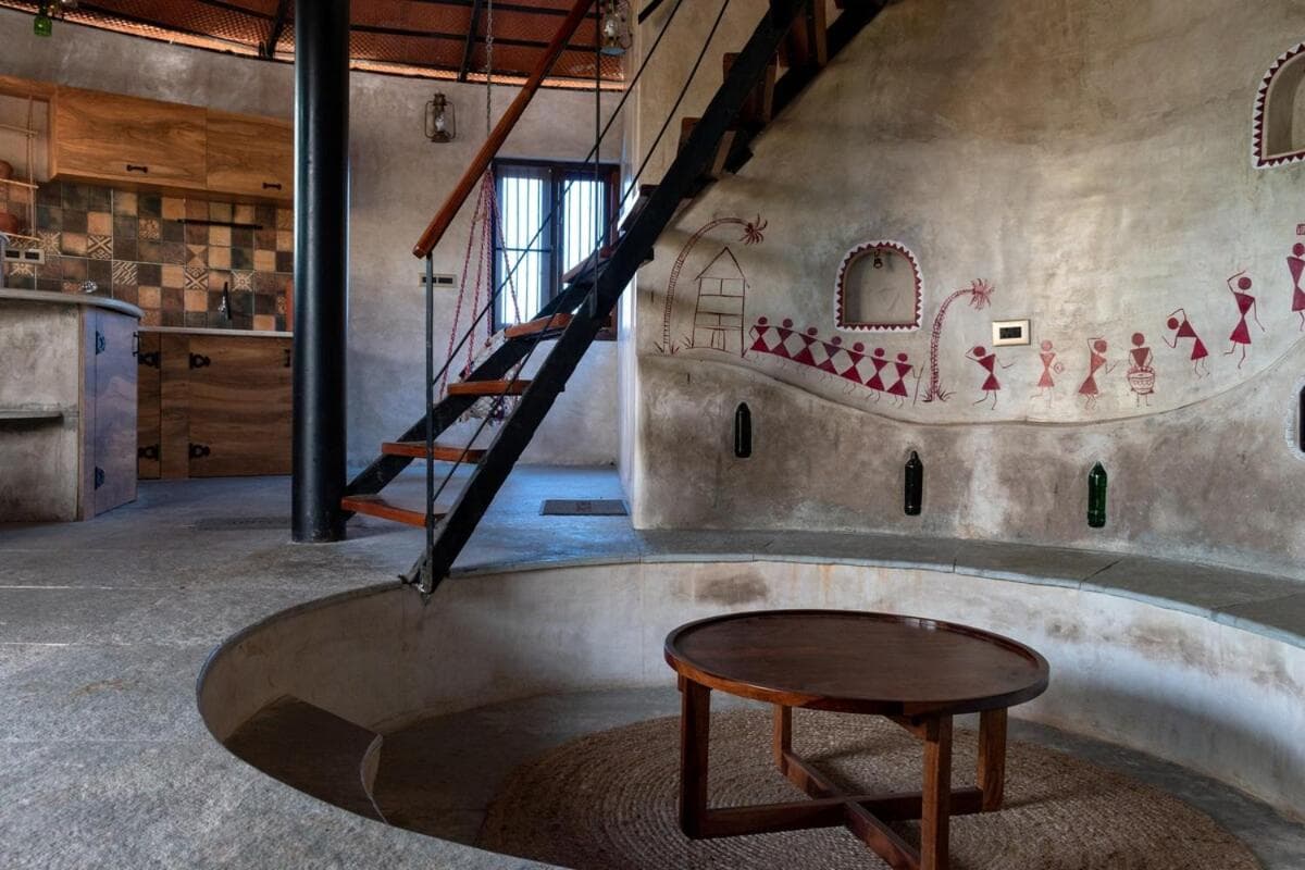 The sunken circular living pit with cushions, a low round table and the spiral stair above