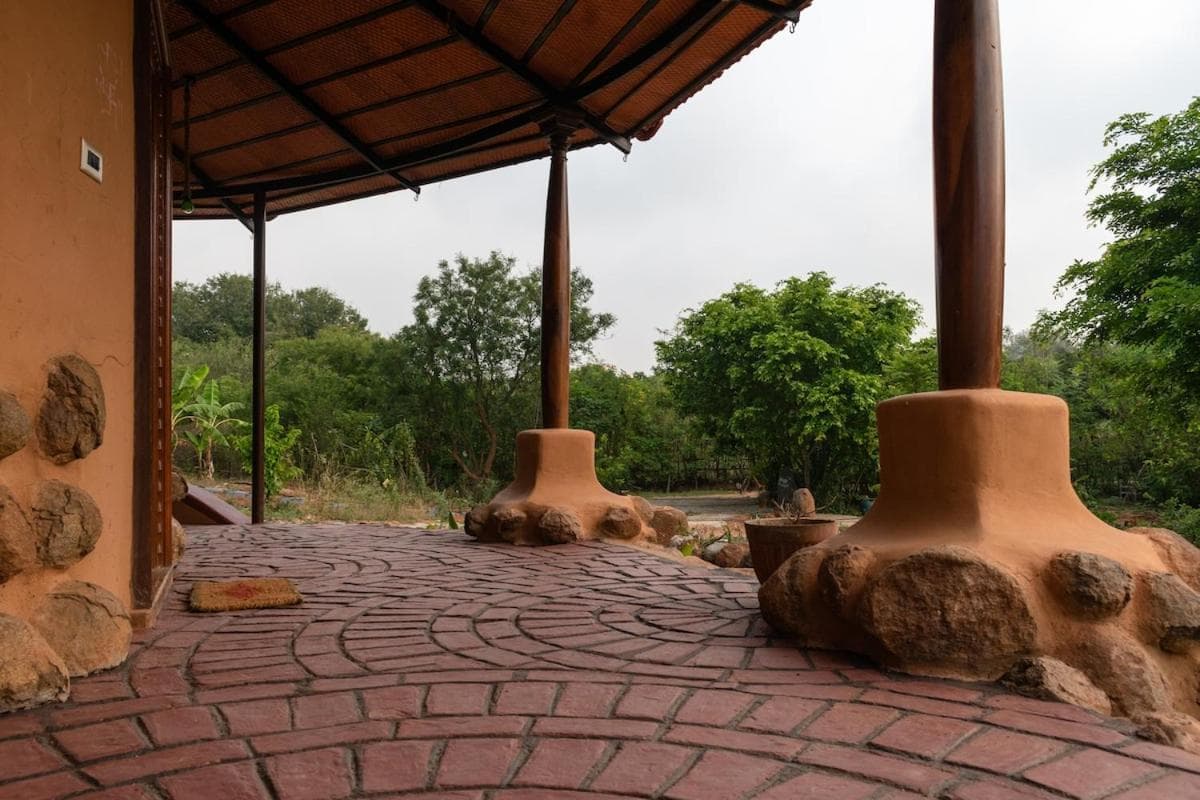 The verandah — a timber pillar on a boulder plinth, stone floor, the scrub beyond