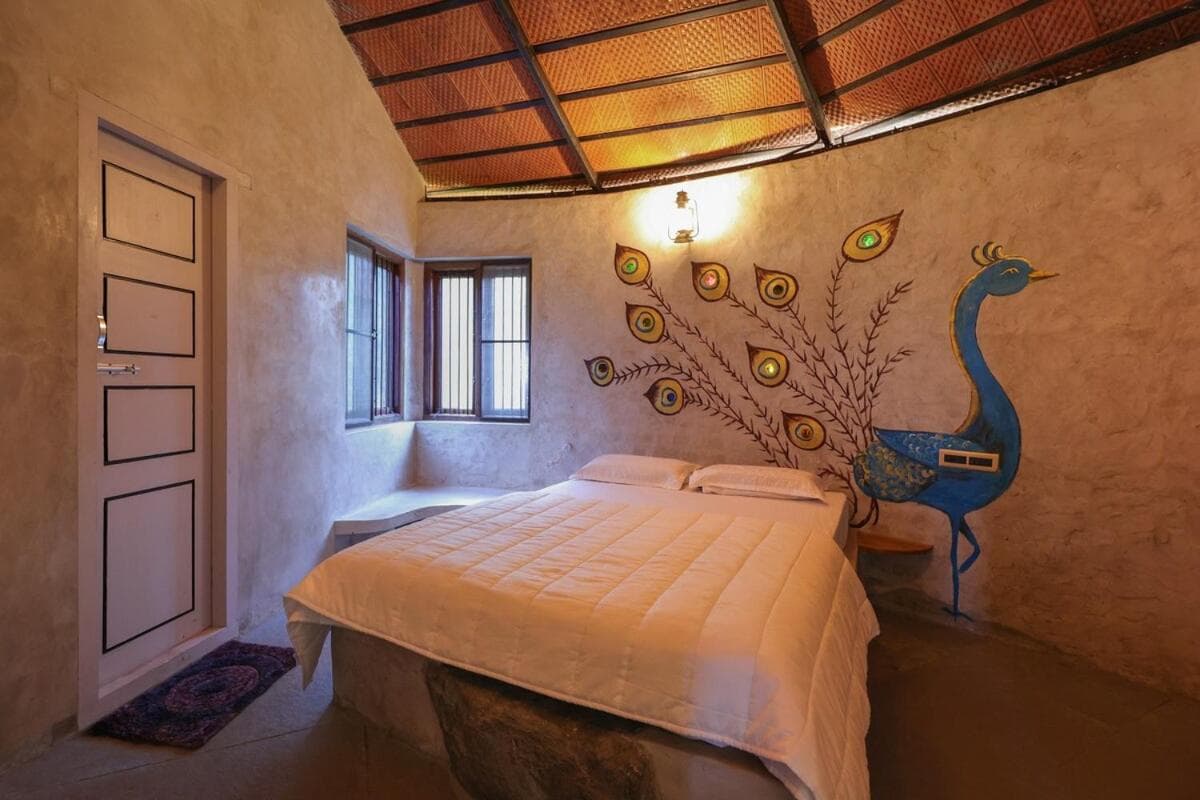 The bedroom — a white double bed under a peacock painted across the earthen wall