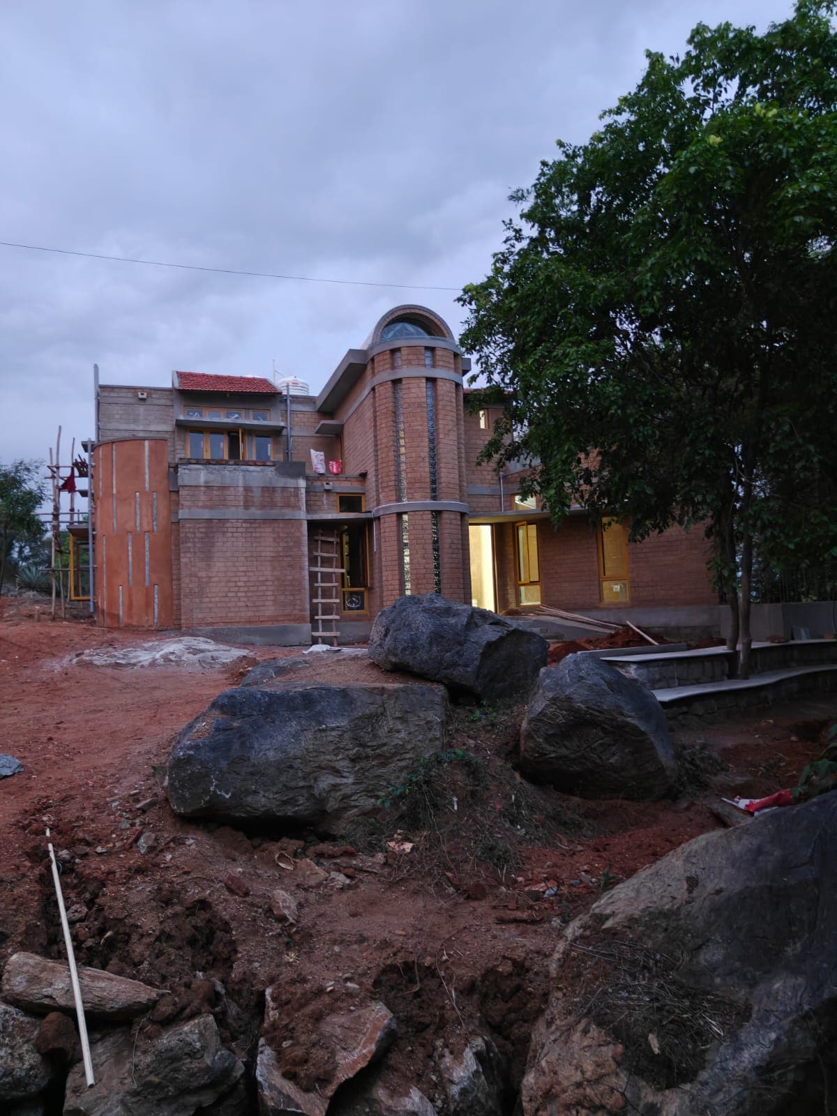 Our new home — handcrafted brick house among rocks and trees, glowing at dusk